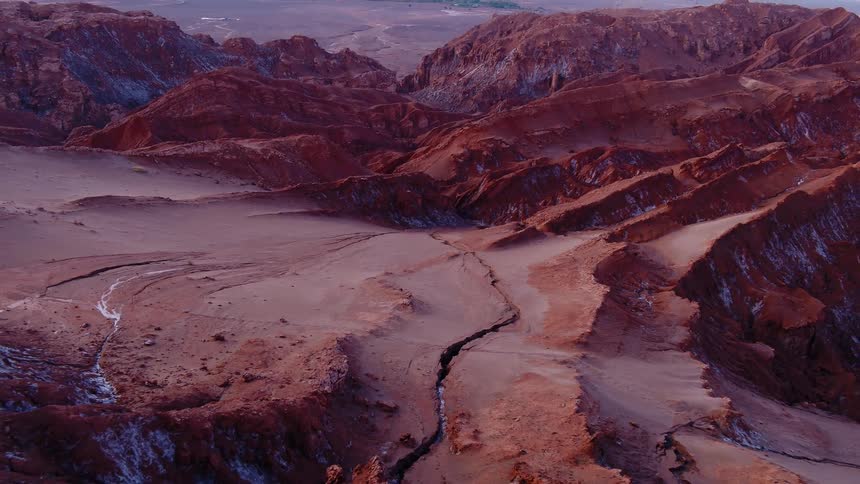 Three people stand on a jagged rocky ridge of a red rock landscape that is still dotted with ice