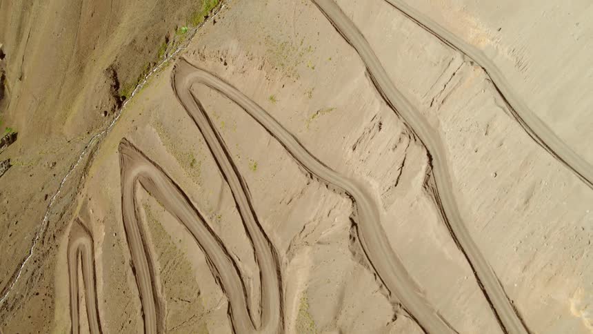 A car traveling along a zigzagging dirt road through a mostly barren landscape