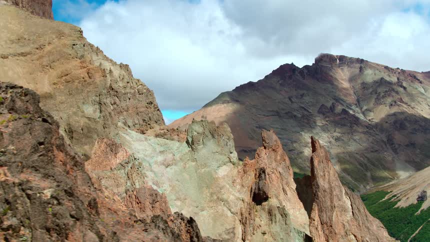 Mountains and rock formations tower over a valley with a forest growing in it