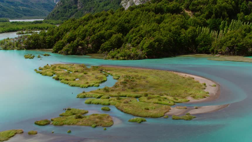 Vegetation covered sandbar island occupies center of azure water near forest and mountains