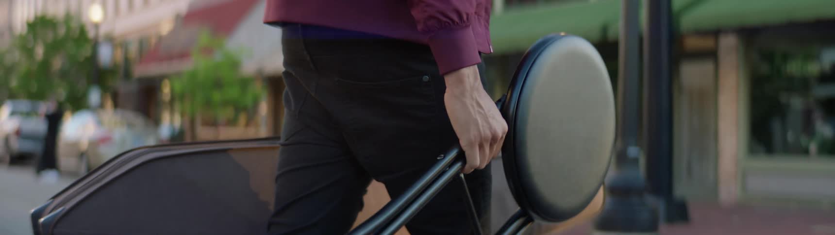 A musician walks across a street carrying his instrument and a stool