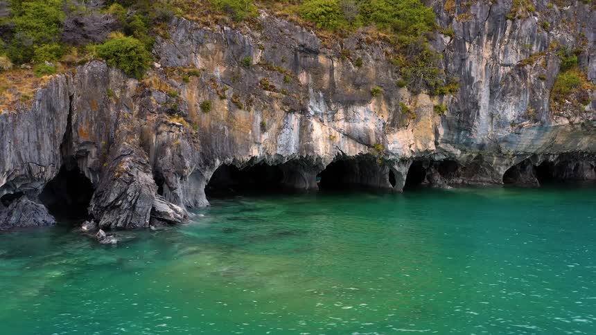 Boat floats in cave at base of vegetation covered cliff