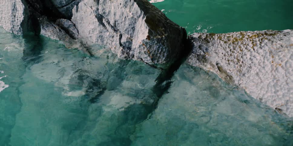 Clear turquoise water laps against rocks with sunlight shimmering on the surface