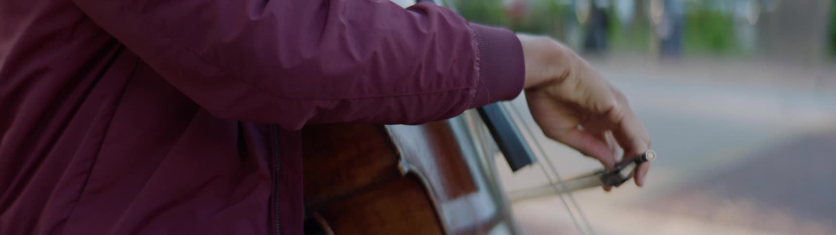A black man sits outdoors in a neighborhood and plays a cello