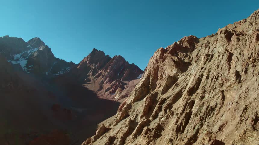 The rocky brown slopes of a narrow mountain valley under a deep blue sky