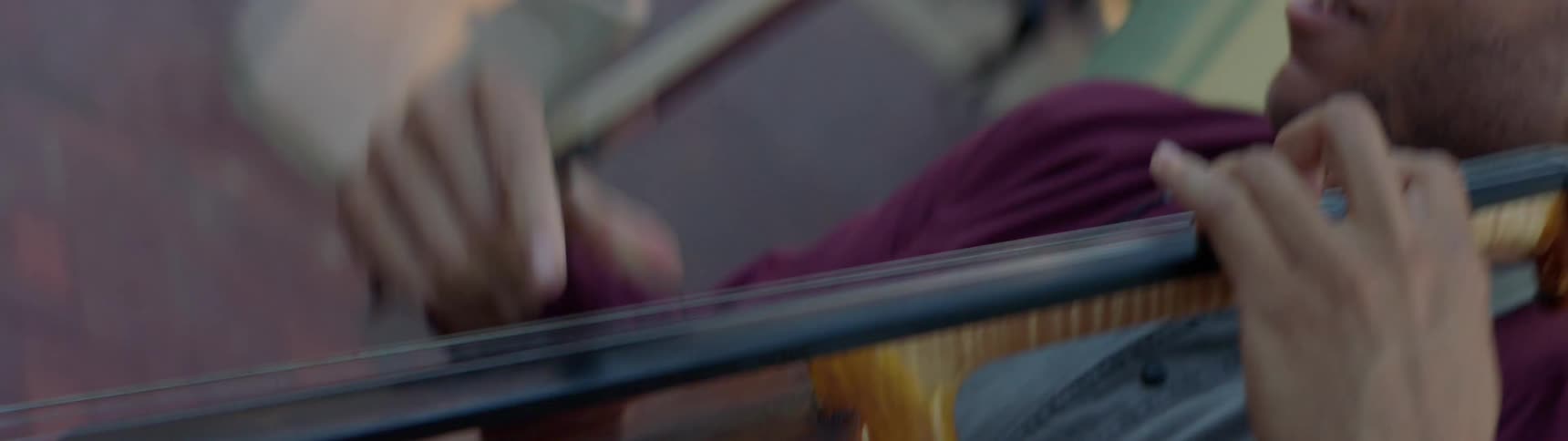 Man plays a musical instrument with a bow while standing outside on a sidewalk