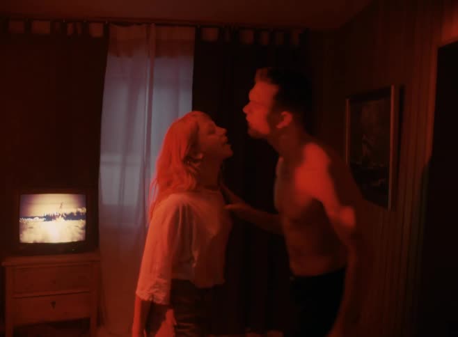 A man shoves a woman as the two argue angrily in a room with red tinted light