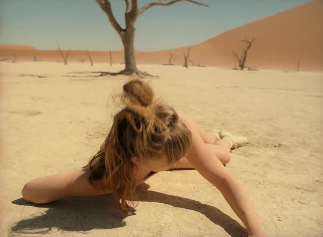 A model writhes around in the desert in a nude colored dress that matches the sand