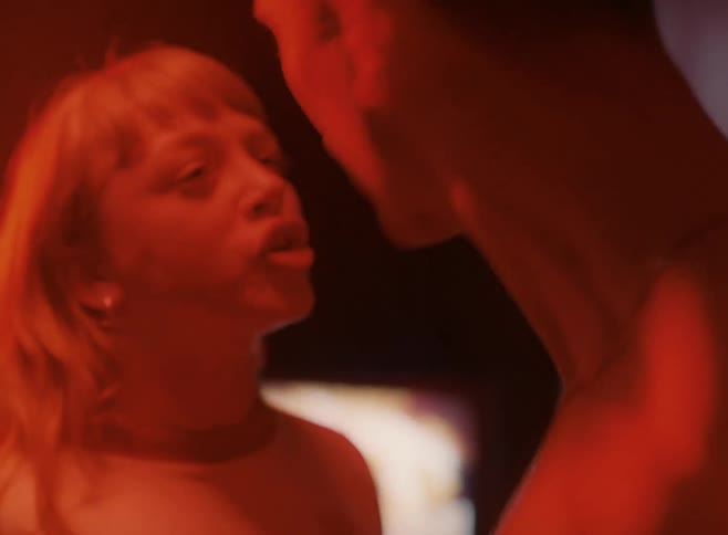 Shirtless man and woman with blonde hair in red light argue furiously in a room