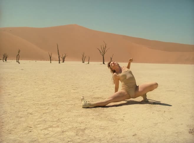 A young woman dancing on flat hardpacked soil in the desert