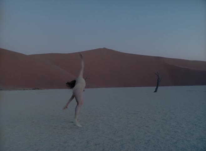 A white woman in a body suit dances in a desert clime