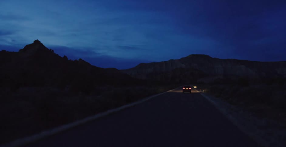 Car travels down the road at night near the mountains