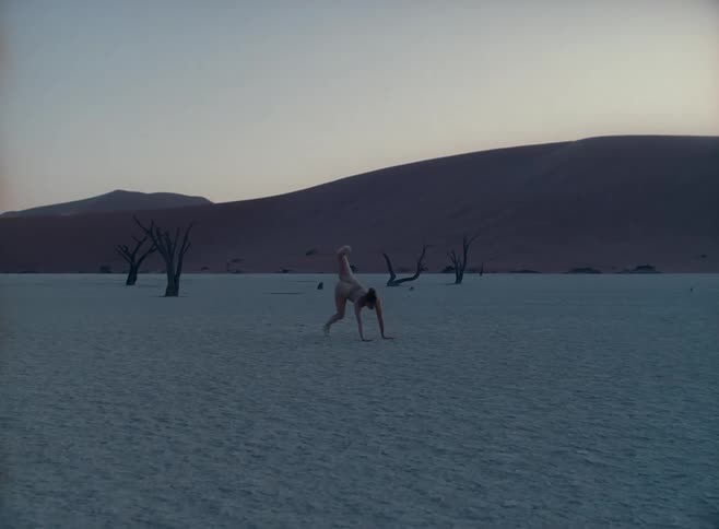 A white woman in a body suit dances in a desert