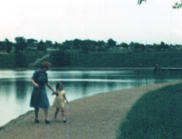 Mother pulling young daughter from edge of lake while strolling on the pathway