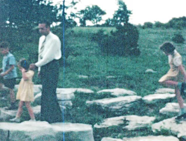 A man a boy and two girls walking on rocks with trees and the sky in the background
