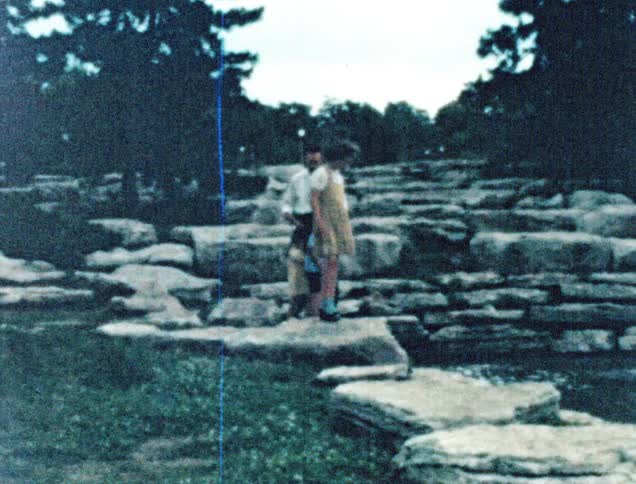 A man and his children hop along rocks next to a river