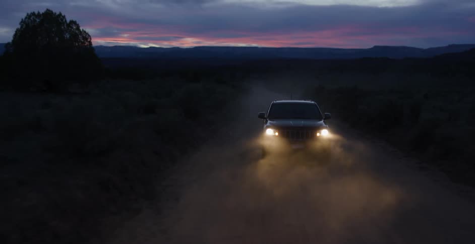 Car illuminating the road ahead by headlights drives on dirt road