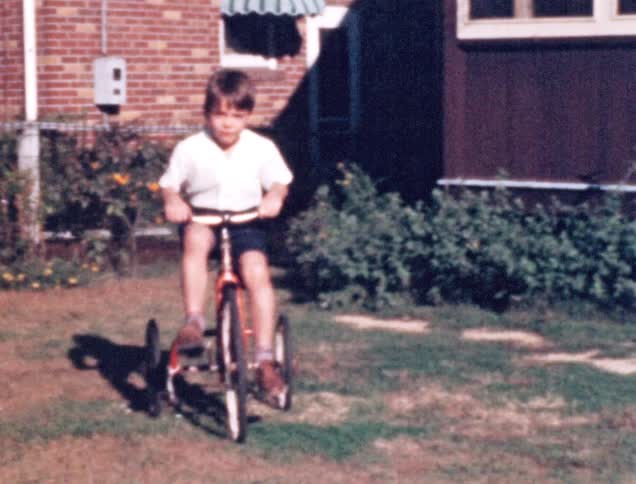 A young boy rides his tricycle through his back yard