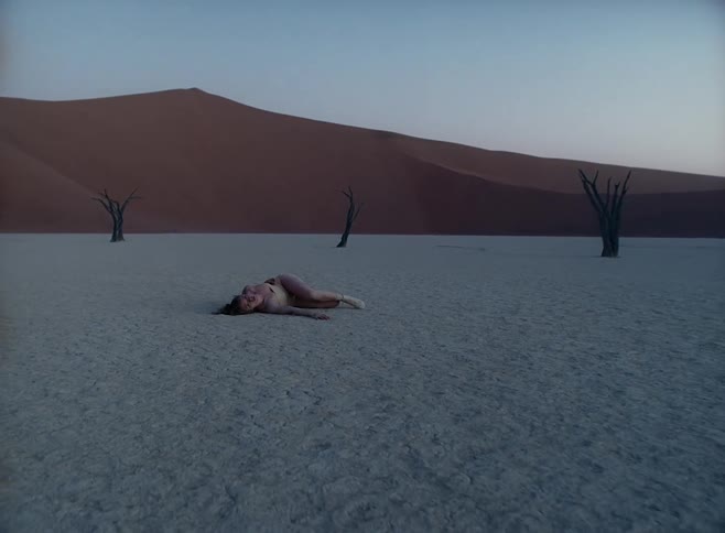 A young white teenager lies on the soil in a desert