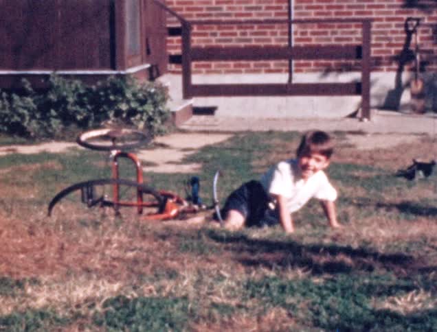 A boy laughs as he falls off his tricycle and gets back up