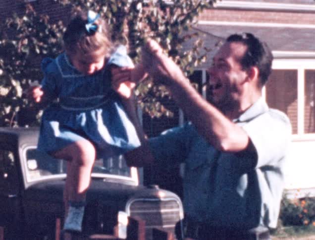 A father helps his young daughter stand upright