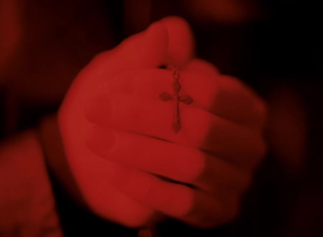 Hands praying holding rosary beads with a gold cross