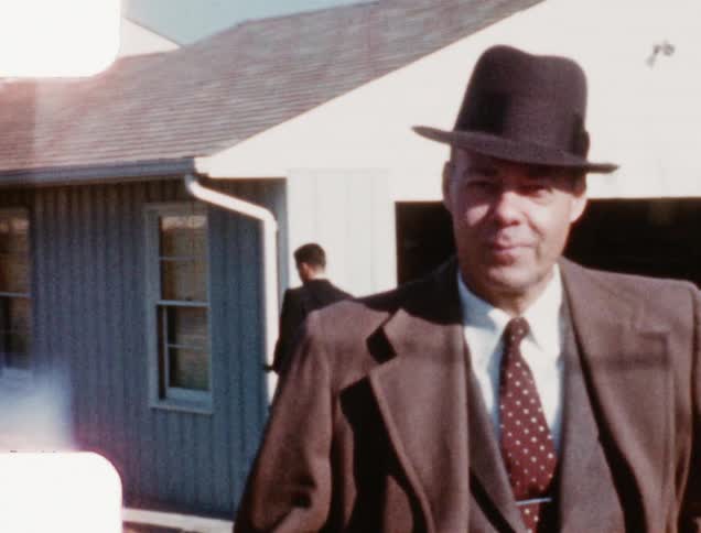 An older white man in a suit speaks to his son who then runs into the house