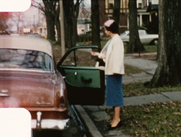 A woman waves at the camera as she waits for another woman to get into the back seat before she gets in the car