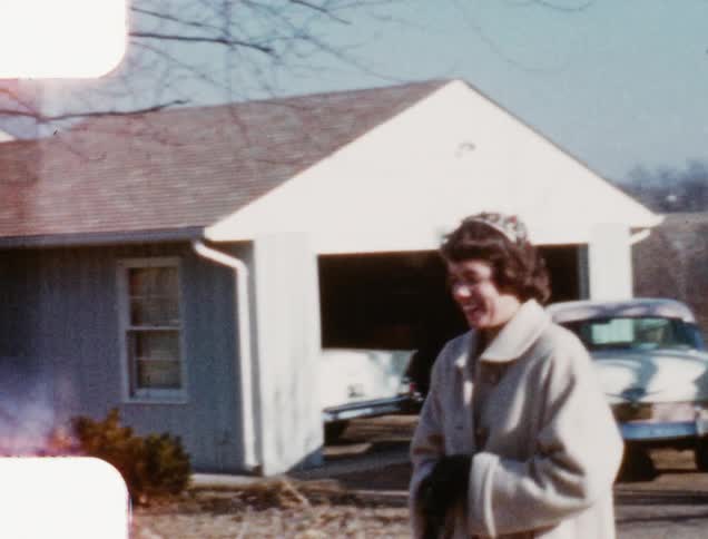A woman with a heavy coat and a small hat smiles as she walks out of her driveway and into the street