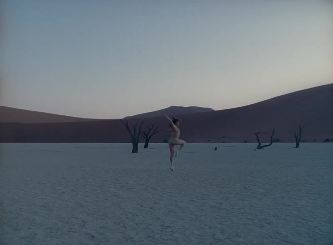 A white woman in a skin colored body suit dances in a desert setting