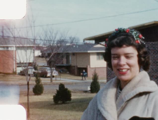 A laughing white woman stands outdoor on a lawn and shows off her handbag with red roses on it