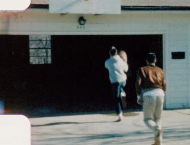 A pair of meaning shooting a basketball at a homemade basketball hoop mounted over the garage of a house