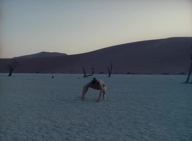 Female dancer dances wildly on sand in desert with dead trees in the background