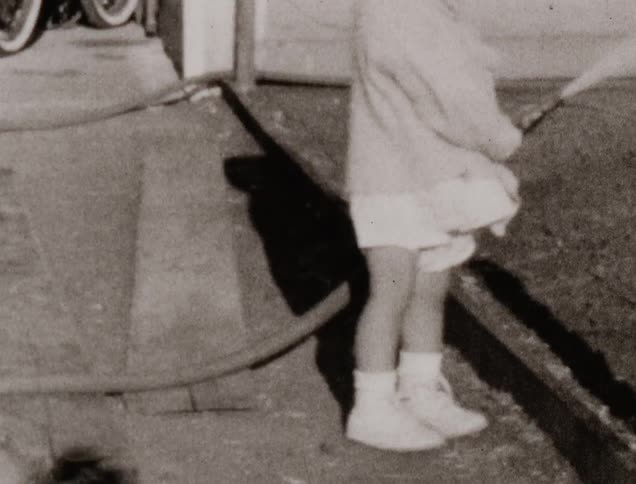 A little girl holds a water hose and waters something