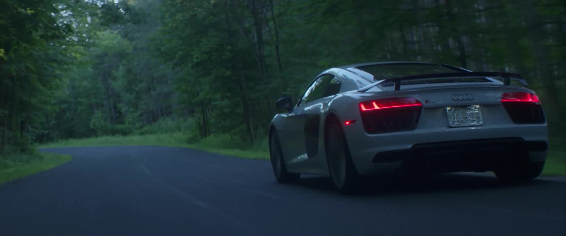 A car is driving down a narrow curving road on a cloudy day