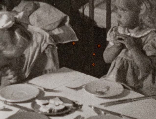 Two female toddlers clasp their hands in prayer as they sit at a dinner table
