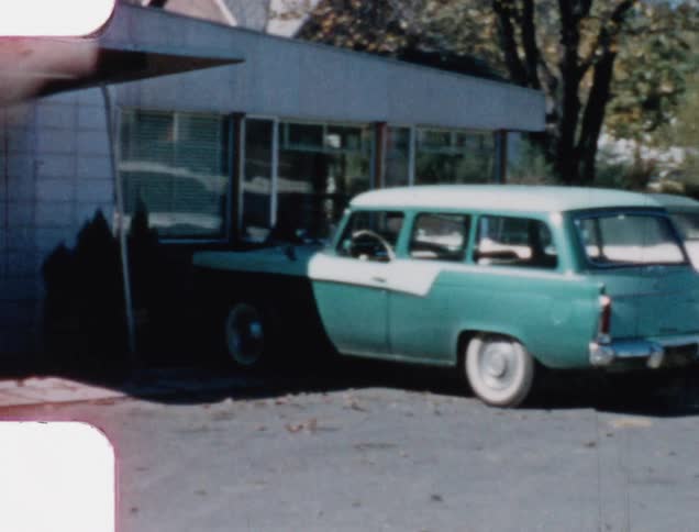 Vintage cars sit in parking lot near awning covered business door