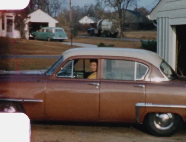 A woman drives a car out of a garage and smiles into the camera