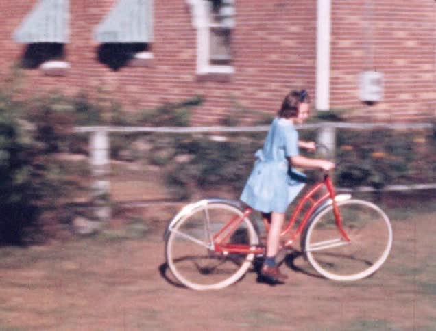 Girl with blue dress rides a red bicycle on the dry grass