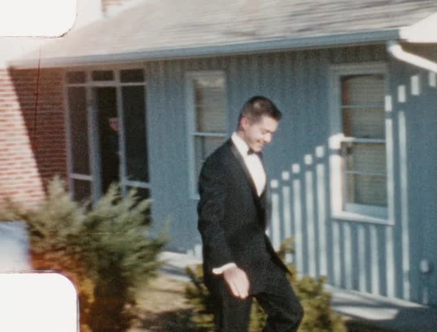 A teenager in a tuxedo waves as he walks toward and opens the door of a vehicle