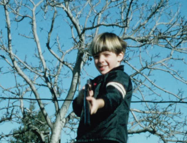 Vintage film of a blonde boy playing with a toy gun outdoors