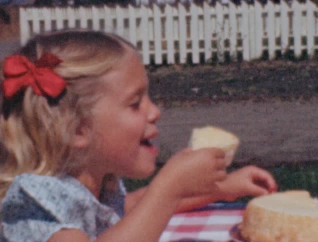 A little blonde girl talks and laughs while holding a piece of cake
