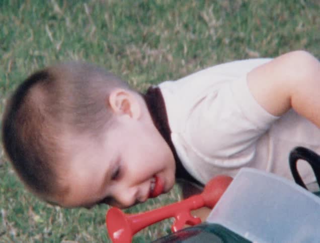 A white boy gets to his feet by a toy car