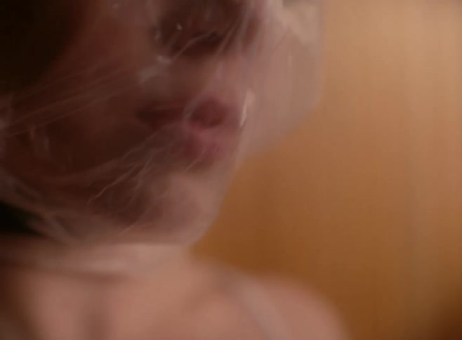 A white woman keeps her eyes closed as she breathes with a plastic bag over her head