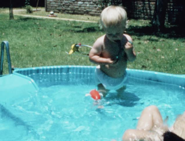 Two young boys splash and play with a toy shark in a kiddie swimming pool