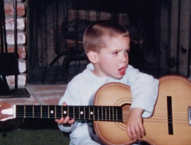 Little child plays a guitar in front of a fireplace in the living room at home