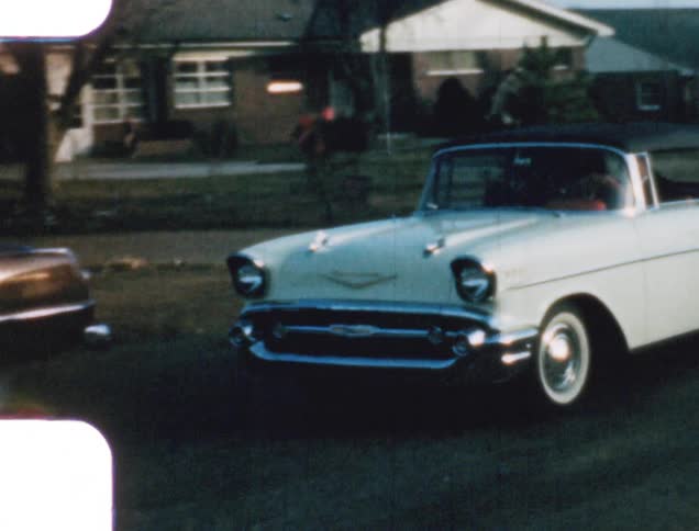A man driving his car waves as he drives down a neighborhood street