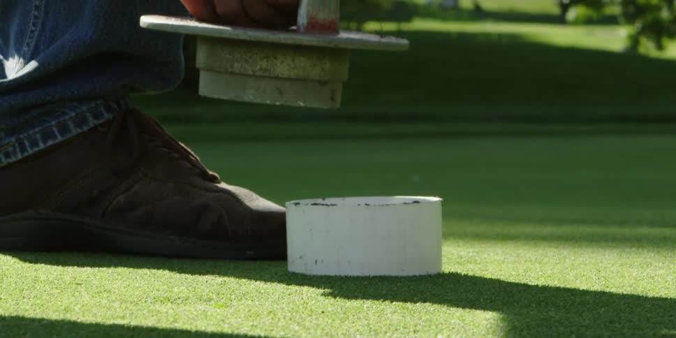Man inserts lidded cylinder in hole on manicured lawn