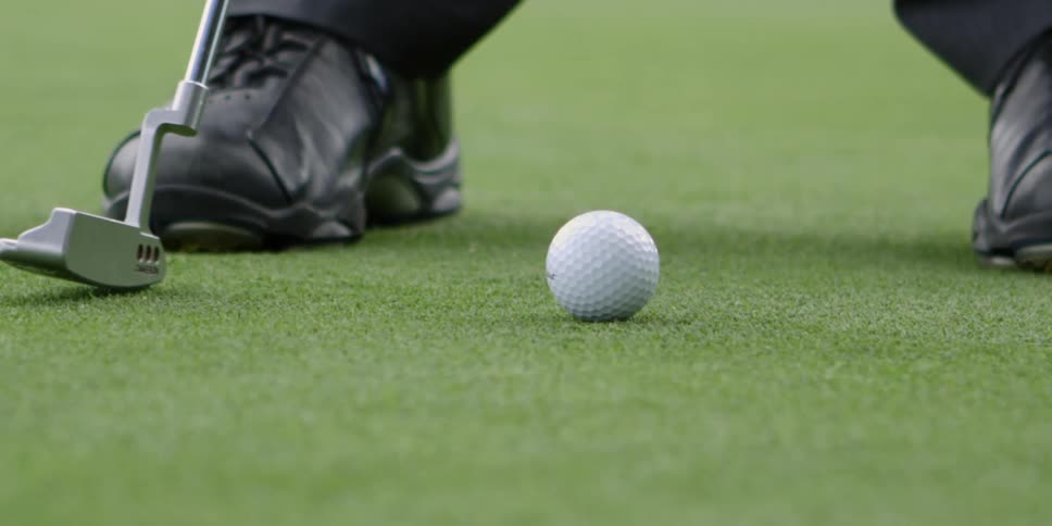 A golfer swings a putter into a golf ball