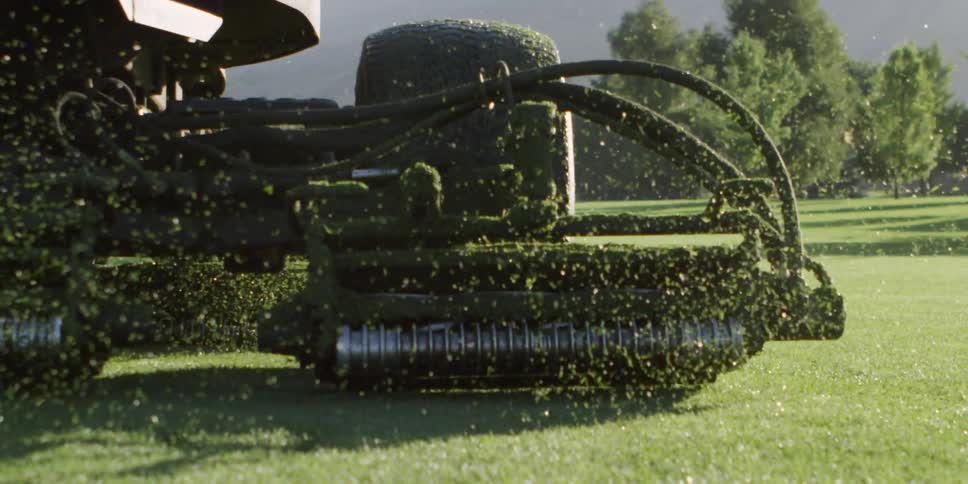 A large riding mower is cutting the grass on the golf course